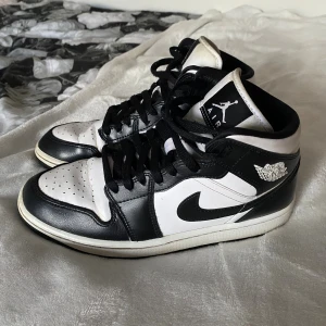 Nike Air Jordan 1 mid  - Nike Air Jordan 1 mid sneakers i svart och vitt. Skorna har snörning bara att jag snörar dem så man slipper knyta. Använda en hel del som man ser under och creasen. Sen är även flärpen lite gul och inte helt vit som man ser på bild 2 och 5. Väldigt fina inut och inget synligt slitage i inner sulan. Köpta på zalando i februari 2024 för 1486kr. 