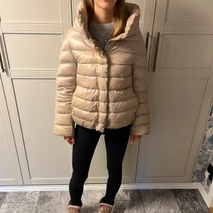 Beige pufferjacka från Herno - Säljer en guld/begie vinterjacka från Herno med hög krage, den är långärmad fast annars samma modell som 3/4ärmande jackorna från herno. Jacka har inga defekter eller skador, Endast tecken på användning. Jacka är i barn storlek 14, men passar som en Damstorlek S. qR-kod och chippet finns kvar i jackan för äkthetsbevis.