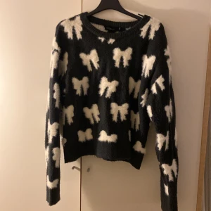 Svart stickad tröja med vita rosetter - Mysig svart stickad tröja från Ullared  i storlek S/ 158/164.Tröjan har ett fluffigt material och är täckt med vita rosett-mönster. Rund halsringning och långa ärmar ger en chill och trendig vibe. Perfekt för dig som gillar att sticka ut med coola detaljer.