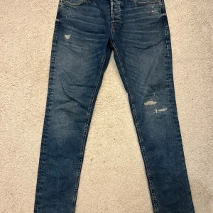 Jack and Jones  jeans - Jack and Jones  jeans med slim passform och klassisk femficksdesign. Jeansen har slitna detaljer framtill för en cool, avslappnad look. Tillverkade i mjukt denimtyg som sitter tajt längs benen.