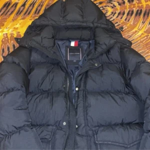 Svart pufferjacka Tommy Hilfiger M - Svart pufferjacka från Tommy Hilfiger i storlek M. Jackan har huva, dragkedja och tryckknappar framtill. Klassisk quiltad design med fyllig look, perfekt för kalla dagar. Snyggt märke på insidan och stilren svart färg. Kan finnas ett litet tecken på användning men inget som syns direkt men därav säljer jag den billigt. Hör av er vid fler frågor och bilder