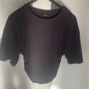 Svart t-shirt med snörning Gina Tricot - Svart t-shirt från Gina Tricot i storlek M. Modellen har korta ärmar, rund halsringning och cool snörningsdetalj i sidan som ger en snygg twist. Tillverkad i mjuk bomull för en skön känsla och avslappnad passform.