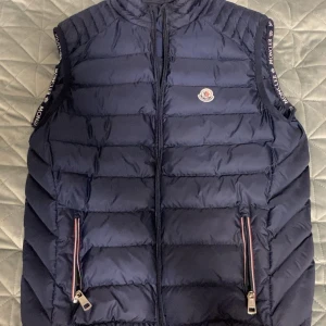 Mörkblå dunväst från Moncler - PRIS KAN DISKUTERAS!😁 Snygg mörkblå dunväst från Moncler med quiltad design och logotyp på bröstet. Västen har dragkedja framtill, två fickor med dragkedja och Moncler-tryck på axelbanden. Insidan har en extra ficka med röd, vit och blå detalj. Perfekt för lager-på-lager.