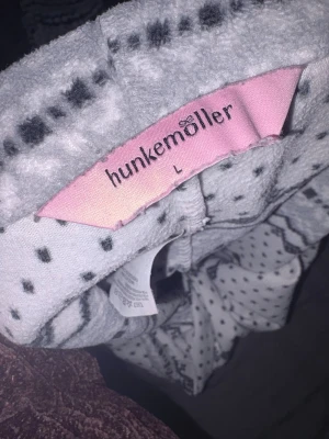 Mjukisbyxor med mönster från Hunkemöller - Supermysiga mjukisbyxor från Hunkemöller i storlek L. Byxorna är vita med grått och svart zigzag- och prickmönster, har en loose passform och är gjorda i mjukt fleece-material. Perfekta för chill hemma och har elastisk midja för extra komfort.