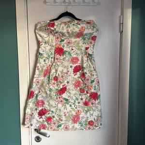 Blommig tubklänning från Old Navy - Säljer en söt tubklänning från Old Navy med blommigt mönster i rosa, rött, grönt och vitt. Klänningen är kort, har smock upptill och dragkedja i sidan för enkel påklädning. Perfekt för dig som gillar färgglada och somriga vibes!