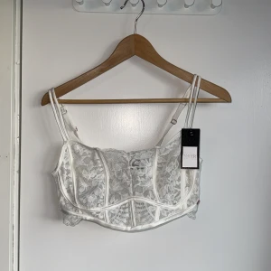 Vit spetskorsett från Hunkemöller - Supersnygg vit korsett från Hunkemöller Noir med blommig spets, dubbla smala axelband och justerbar knäppning bak. Detaljerad med genomskinlig spets och markerade sömmar för en trendig look. Perfekt för dig som vill sticka ut. Oanvänd, nypris 489kr