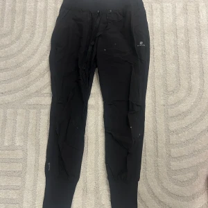 Svarta mjukisbyxor från Domyos - Det vita prickarna är katt hår, men tvättar dom såklart innna jag skickat! Svarta mjukisbyxor från Domyos med elastisk midja och snörning. Byxorna har ribbade muddar vid bensluten och är tillverkade i mjukt material som passar perfekt för chill eller träning. Snyggt tryck med Domyos-loggan på benet.