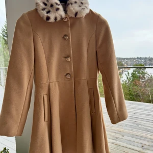 Beige kappa med pälsdetalj! 🌟💫 - Snygg beige kappa med knappar framtill och två fickor. Kragen har en fluffig pälsdetalj med svartprickigt mönster som ger en cool vintagevibe. Kappan har lång ärm och en klassisk, lite utsvängd siluett. Perfekt för dig som gillar stilrena och unika plagg. 🤎🤎 skriv gärna vid funderingar och intresse! 🌟💫