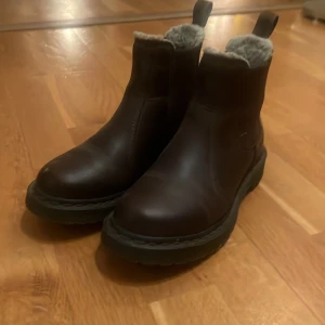Dr. Martens bruna fodrade boots - Säljer ett par bruna Dr. Martens boots i skinn med varm, ljus fuskpäls på insidan. Rejäl sula med bra grepp och klassisk Dr. Martens-detalj baktill. Använda men i fint skick. 