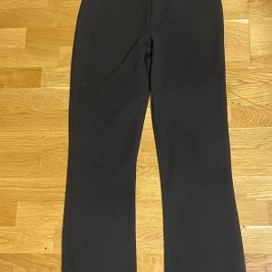Svarta bootcut kostymbyxor - Snygga svarta kostymbyxor med bootcut-snitt som ger en schysst siluett. Byxorna har en klassisk rak midja och är tillverkade i ett mjukt material som känns bekvämt hela dagen. Perfekta för dig som gillar stilrena och tidlösa plagg.