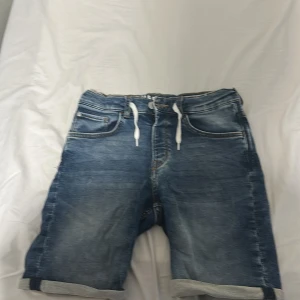 Slim fit denimshorts SUPERSOFT - Snygga blå denimshorts från H&M med slim fit-passform och vit snörning i midjan. Shortsen har klassiska fem fickor, uppvikta benslut och coola kontrastsömmar. SUPERSOFT-materialet gör dem extra sköna att bära hela sommaren.