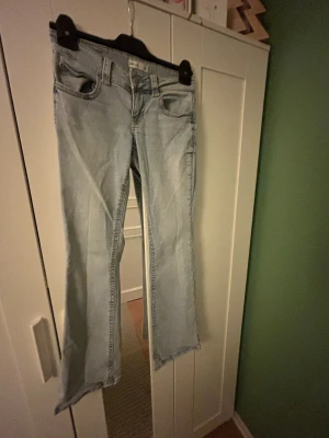 Bootcut ljusblå jeans från ginatricot - Snygga ljusblå bootcut jeans från Gina Tricot  i storlek 36. Jeansen har klassisk femficksdesign, låg midja och råa kanter vid bensluten för en cool vibe. Tillverkade i mjukt denim med dragkedja och knapp framtill.