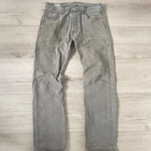 Grå Levi's 501 jeans W32 L32 - Säljer ett par klassiska grå Levi's 501 jeans med raka ben och fem fickor. Jeansen har knappgylf, silverfärgade nitar och den ikoniska läderpatchen bak i midjan. Passar dig som gillar tidlös stil och vill ha ett par jeans med snygg vintagekänsla. Skriv för fler bilder med mera