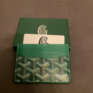 Grön G plånbok med mönster - Snygg grön plånbok  med grafiskt mönster i vitt och brunt. Plånboken är i smidig modell för kort och är tillverkad i skinn med präglad logotyp upptill. Perfekt accessoar för dig som gillar exklusiva detaljer.