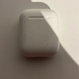 AirPods 2 - Apple AirPods 2 med laddningsetui. Trådlösa hörlurar med enkel anslutning till iPhone och andra Apple-enheter. Skick: synligt smuts och slitage på etuiets insida och utsida, men fungerar. Perfekt för dig som vill ha prisvärda AirPods.