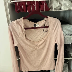Ljusrosa långärmad topp - Säljer en ljusrosa långärmad topp från Divided med fyrkantig ringning och spetsdetaljer längs kanten. En julklapp som aldrig  kom till användning.