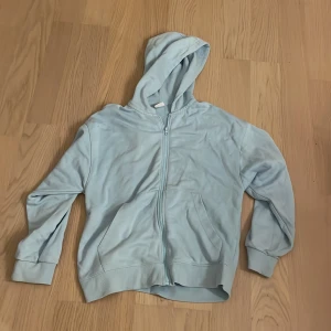 Ljusblå hoodie från Zara med dragkedja - Snygg ljusblå hoodie från Zara i storlek 164. Tröjan har huva, långa ärmar och praktisk dragkedja framtill. Tillverkad i mjuk bomull och har två fickor på framsidan. Perfekt för chill dagar och enkel att matcha med jeans eller joggers.