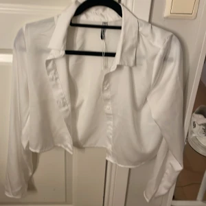 Vit croppad skjorta från FB Sister - Snygg vit croppad skjorta från FB Sister i storlek XS. Skjortan har klassisk krage, långa ärmar och knappar framtill. Materialet känns mjukt och lätt, perfekt för dig som gillar stilrena och trendiga plagg med en modern twist. Den är lite mer liknande en magtröja för att den är rätt så kort.🤗
