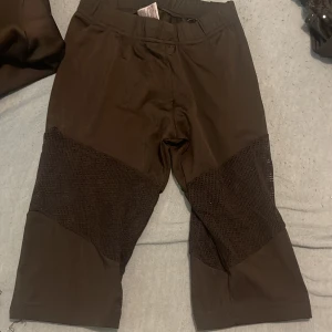 Svarta cykelshorts med meshdetaljer - Säljer ett par svarta cykelshorts med coola meshpaneler över låren. De har en tight passform och är perfekta för träning eller när du vill ha en sportig vibe. Materialet känns stretchigt och bekvämt, och midjan är normalhög för en skön känsla.