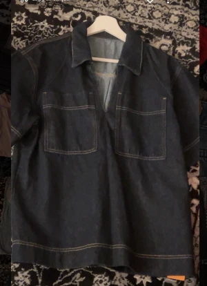 Mörkblå denim henley  - Snygg mörkblå henley med två stora bröstfickor och kontrastsömmar. Skjortan har korta ärmar, klassisk krage och är gjord i kraftig denim med en loose passform. Perfekt för dig som gillar street och enkel stil.helt nytt.priset gör att diskuteras vid en snabb äffar