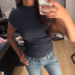 Polotopp - Säljer en stilren mörkblå polotopp från 157 i storlek XS. Toppen har korta ärmar och en högre krage. Passformen är slim och toppen är enfärgad utan mönster.