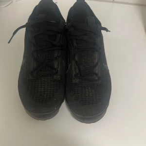 Svarta Nike Vapormax sneakers - Säljer ett par helsvarta Nike Vapormax sneakers med stickad ovandel och klassisk swoosh på sidan. Skorna har snörning och den ikoniska genomskinliga bubbliga sulan som ger grym komfort och cool look. Perfekta för dig som gillar sportig stil och vill ha något som sticker ut.