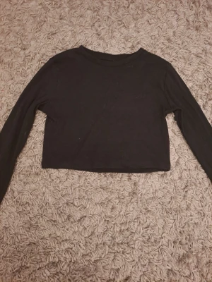 Svart croppad långärmad topp H&M - En svart, croppad långärmad topp från H&M. Enkel och stilren design med rund halsringning och tight passform. Perfekt att matcha med höga jeans eller kjol. Tillverkad i mjuk bomull för en bekväm känsla.