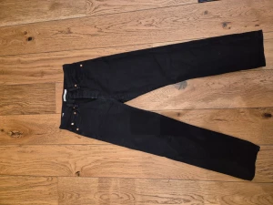 Levi's Wedgie Straight svarta jeans - Svarta jeans från Levi's i modellen Wedgie Straight. Klassisk femficksdesign med raka ben och hög midja. Jeansen har silverfärgade knappar och är tillverkade i bomull med en liten del elastan för extra komfort. Perfekt för dig som gillar en clean och tidlös look.