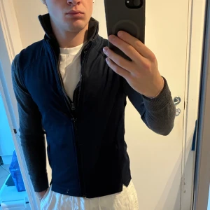 Mörkblå sportväst från Puma - Snygg mörkblå sportväst från Puma med hög krage och hel dragkedja framtill. Västen har två praktiska fickor med dragkedja och är tillverkad i ett mjukt syntetmaterial som passar perfekt för golf eller andra utomhusaktiviteter. Stilren och funktionell design. Sitter som XS. Västen är omsydd hos skräddare för bättre passform.