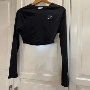 Svart croppad långärmad topp Gymshark - Säljer en svart croppad långärmad topp från Gymshark med vit logga på bröstet. Använd enstaka gång. Nypris 349kr.