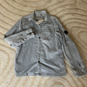 CP company overshirt - Tja! Säljer nu denna jättefina och stilrena overshirt i babyblå färg från CP company. Vill du ha något som sticker ut lite extra eller bara rocka de en fredag i skolan med skjorta under är detta verkligen något för dig. 10/10 skick då den är helt ny med tag på nypris ligger på runt 3500 men mitt är endast 1299! Säljes då den tyvärr inte passar. Storleken är L men passar både L och större M. Vid frågor eller funderingar kontakt gärna mig. Skynda fynda! MVH Viken!