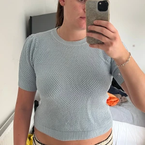 Ljusblå stickad croppad topp - Säljer en ljusblå stickad topp med korta ärmar och rund hals. Toppen är croppad och har ett snyggt, strukturerat stickat mönster över hela plagget. Perfekt för dig som gillar en enkel men ändå trendig look.
