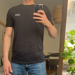 Svart Hugo Boss t-shirt med logga - Svart t-shirt från Hugo Boss med vit logotyp på bröstet. Klassisk rund hals och korta ärmar. T-shirten är gjord i mjuk bomull och har en clean, stilren look som funkar till jeans mm