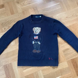 Ralph Lauren polo bear knit  - Mörkblå stickad tröja från Polo Ralph Lauren med ikoniska Polo Bear-motivet framtill. Tröjan är i 9/10 skick men har en liten fläck på mitten som inte syns i verkligheten, ser mycket sämre ut på bild. Storlek S. Hör av dig vid minsta fundering 