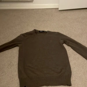 Brun stickad tröja från J.Lindeberg - Säljer en brun stickad tröja från J.Lindeberg i storlek XS. Tröjan har v-ringning, långa ärmar och en liten broderad logga på bröstet. Perfekt för lager-på-lager och passar till både jeans och chinos.