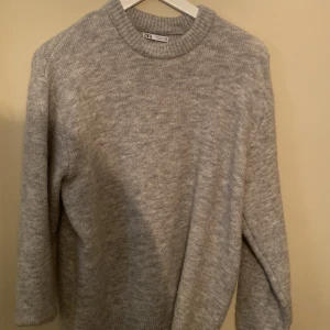 Grå stickad tröja från Zara - Mysig grå stickad tröja från Zara i storlek S. Tröjan har rund halsringning, ribbade muddar och en klassisk, enkel design som passar perfekt till jeans eller kostymbyxor. Skön och varm för kyligare dagar. Nästan helt oanvänd.