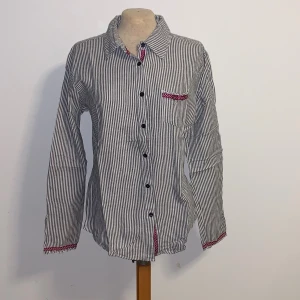 Randig skjorta Esprit de Corp - Snygg skjorta från Esprit de Corp med smala svarta och vita ränder. Långa ärmar och svarta knappar framtill. Fina detaljer i rödprickigt tyg vid krage, knappslå och bröstficka. Skön bomullskänsla och klassisk passform. Står ingen storlek men gissar på S.