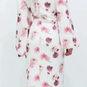 Blommig långklänning från Gina Tricot -  långklänning från Gina Tricot i vitt med rosa och lila blommönster. Klänningen har v-ringning, långa vida ärmar och knappar framtill samt en slits. Den kommer ej till användning men har används 2 gånger 