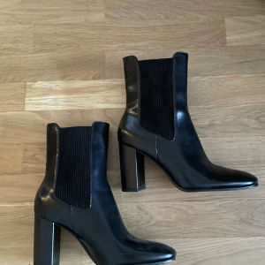 Svarta boots - Snygga svarta chelsea boots i skinn med hög klack och rund tå. Klassisk design med elastiska paneler på sidorna som gör dem enkla att ta på. Perfekta för dig som vill ha en stilren och trendig look. 