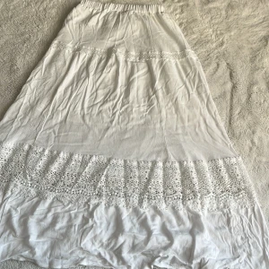 Vit långkjol med spets från SHEIN - Superfin vit långkjol från SHEIN med bred spetsvolang nertill och elastisk midja. Kjolen är luftig och har en romantisk vibe med snygga spetsdetaljer som gör den extra söt. Perfekt för dig som gillar en boho-stil och vill ha något lätt till sommaren.