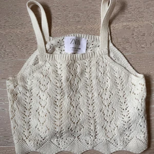 Stickad linnetopp från Zara i vitt - Supersöt stickad linnetopp från Zara i vit färg. Toppen har smala axelband och ett fint hålstickat mönster över hela plagget samt vågig kant nedtill. Perfekt för varma dagar och enkel att matcha med jeans eller kjol.