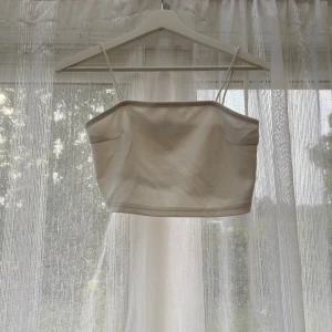 Beige vit croppad linnetopp - Snygg beige croppad linnetopp med tunna axelband. Enkel och stilren design som passar perfekt till varma dagar. Toppen har en rak form och är tillverkad i ett lätt material som känns skönt mot huden. Passar XS/S