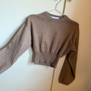 Beige croppad tröja från Bershka - Säljer en beige/brun croppad tröja från Bershka med ribbad midja och rund halsringning. Tröjan har långa ärmar och är gjord i mjukt stickat material, den är helt ny med prislapp.