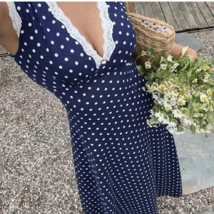 Marinblå prickig långklänning med spets - Superfin marinblå långklänning med vita prickar och v-ringning kantad av vit spets. Klänningen är ärmlös och har en figurnära passform upptill som faller snyggt över kroppen. Perfekt för sommarens och höstens alla tillfällen! Tänk er en picknick med med någon ni gillar eller kanske en dejt...😉 det finns även en liten blomma i v ringningen slut. Så gulligt♡♡♡ Den är aldrig använd och själ allas uppmärksamhet!! 💐💐 priset kan diskuteras!! 