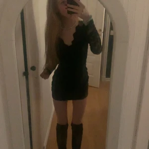 Svart spetströja med lång ärm - Supersnygg svart långarmad tröja med långa spetsärmar och v-ringad halsringning med vågig kant. tröjanhar en tight passform och är perfekt för dig som vill sticka ut. Materialet är troligtvis polyester eller liknande för stretch och komfort.