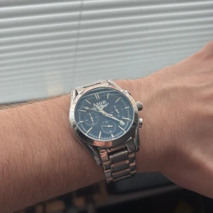 Silverfärgad klocka från LIGE - Snygg silverfärgad klocka från LIGE med en stilren blå urtavla och tre mindre sub-dials. Armbandet är i rostfritt stål och har en klassisk länkdesign. Perfekt för den som gillar en elegant och tidlös stil.