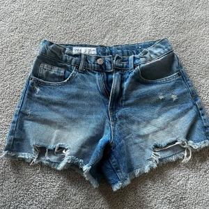 Blå jeansshorts från Zara - Snygga blå jeansshorts från Zara med slitna detaljer och fransig kant nertill. Klassisk femficksmodell med knapp och dragkedja framtill. Perfekta för en chill sommarlook och passar till allt. Materialet är robust denim som håller stilen hela dagen.