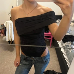 Svart offshoulder body - Säljer en svart, tight offshoulder body med snygg drapering och omlottkänsla. Perfekt att styla med jeans eller kjol för en stilren outfit. PRIS GÅR ATT DISKUTERA 