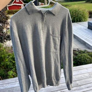 Grå halvzip stickad tröja - Snygg grå stickad tröja med halv dragkedja och klassisk krage. Tröjan har en liten bröstficka och långa ärmar, perfekt för lager-på-lager. Enkel och stilren design som funkar till många outfits. Priset är ej hugget i sten😊