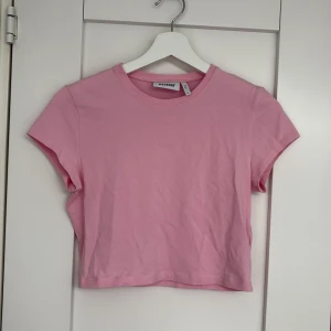 Rosa croppad topp från Weekday - En enkel och croppad topp från Weekday i en superfin rosa färg. T-shirten har rund halsringning, korta ärmar och är gjord i mjuk bomull. Perfekt att matcha med jeans eller kjol för en chill look.